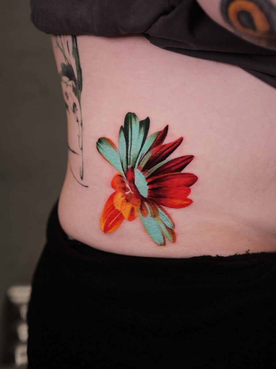 This belly tattoo features a flower design, showing a blend of red, orange, and teal hues.