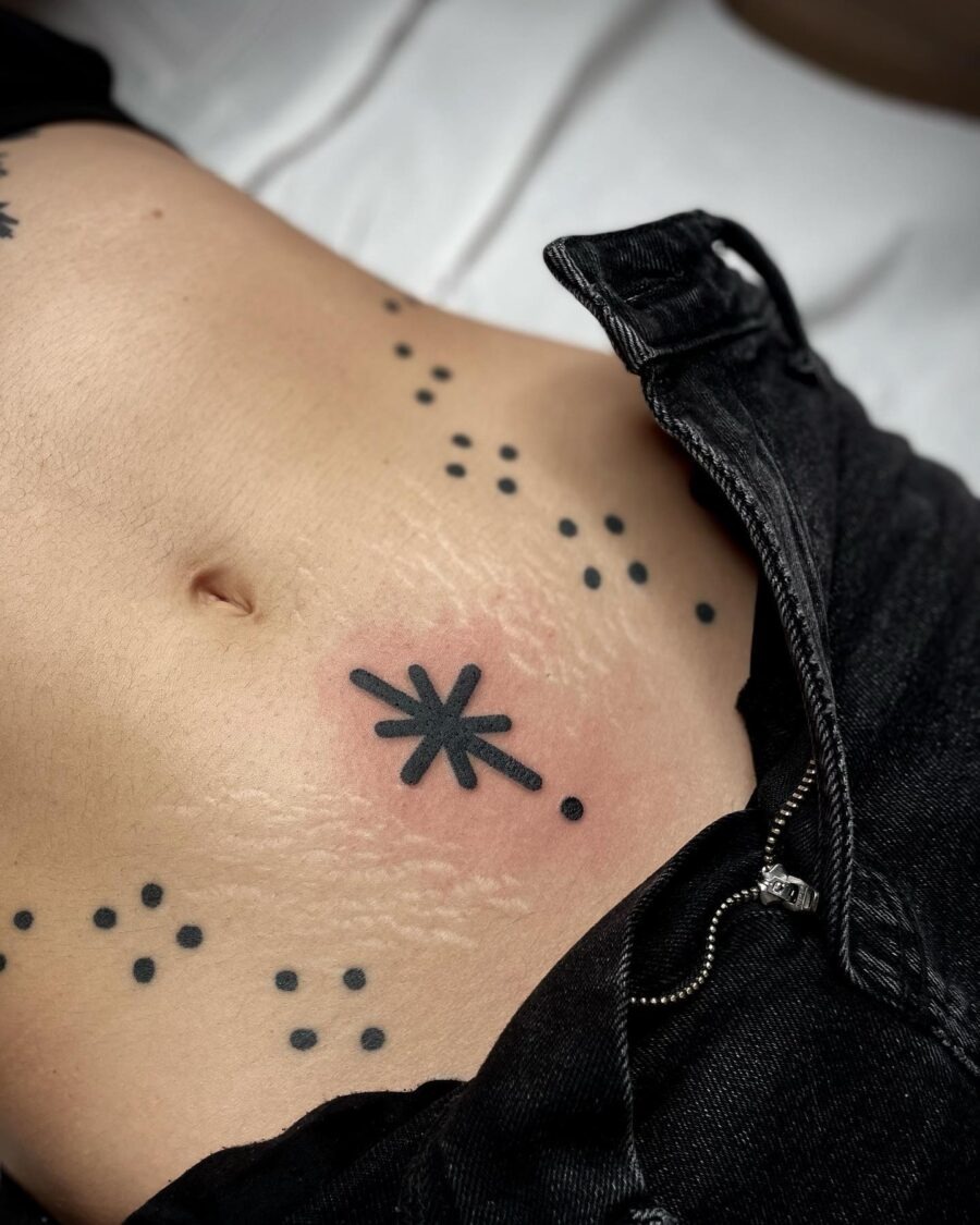 This belly tattoo features a striking starburst design adorned with delicate dot accents, creating a captivating focal point.