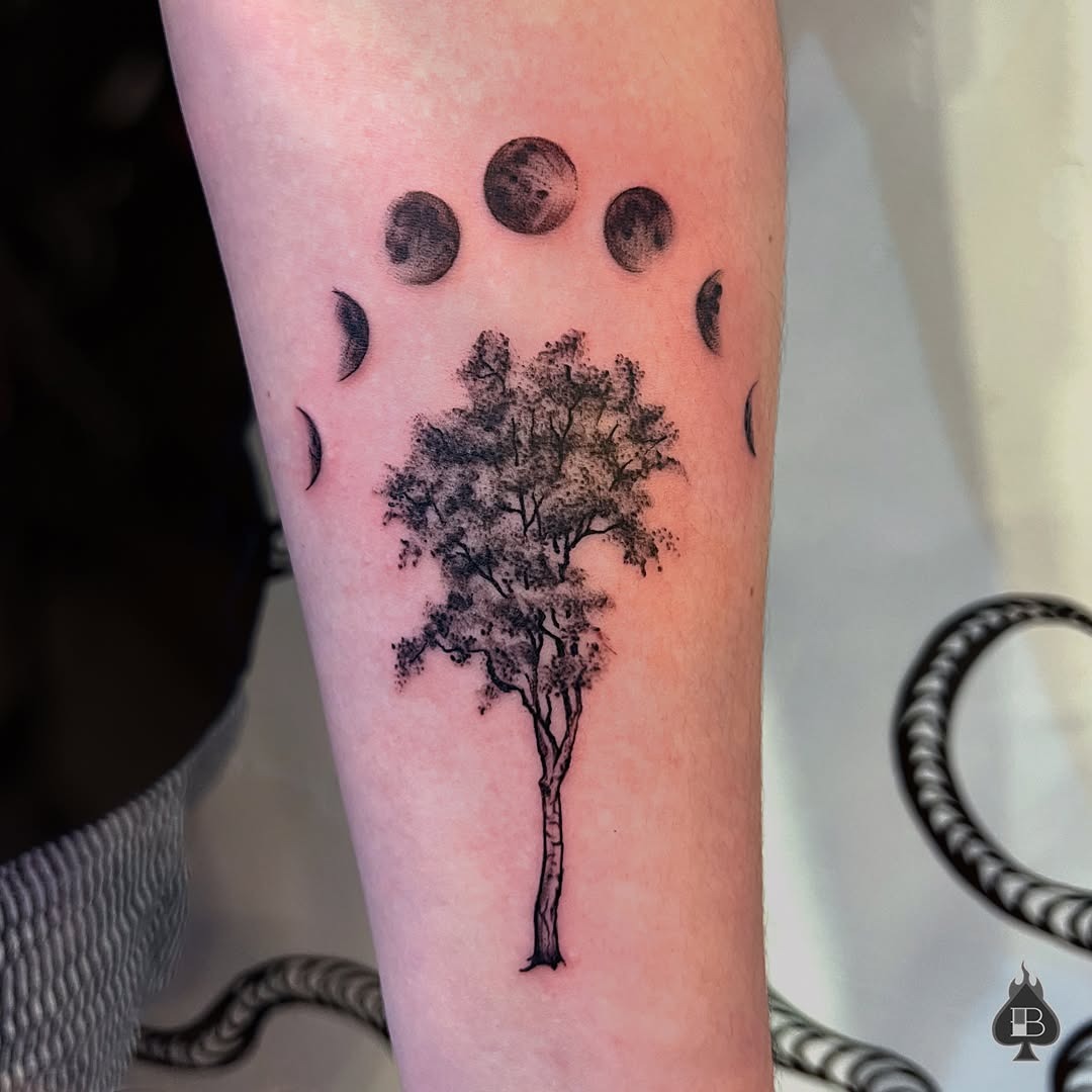This tattoo features a detailed birch tree surrounded by moon phases, creating a mystical vibe.