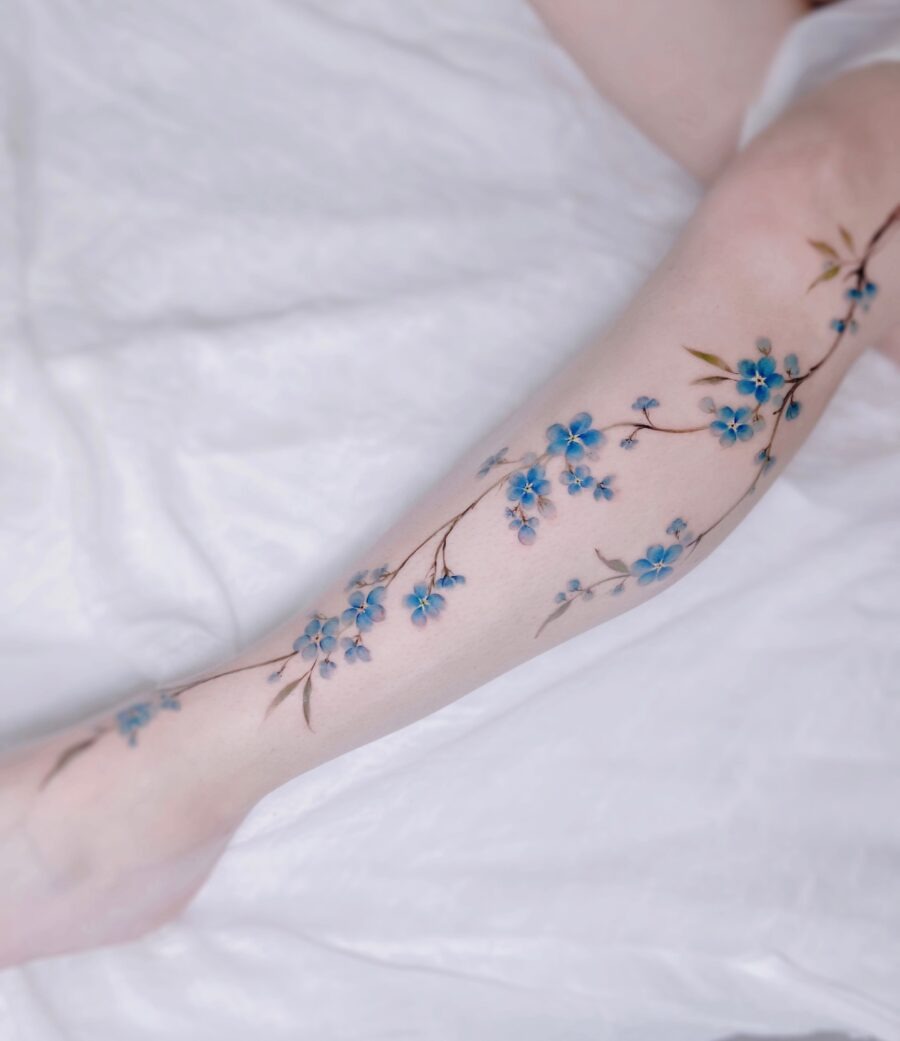 This stunning tattoo features delicate blue flowers gracefully vine-like along the arm.