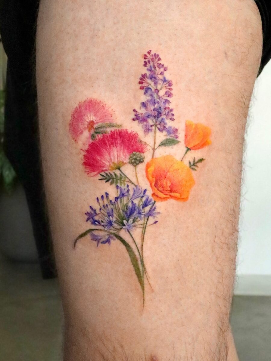This tattoo showcases a stunning arrangement of various colorful flowers, including soft pinks and radiant oranges.