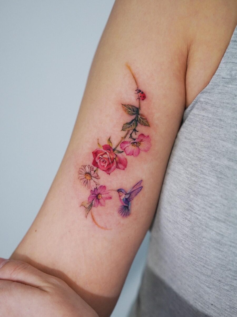 This tattoo features an elegant composition of blooming flowers and a hummingbird.