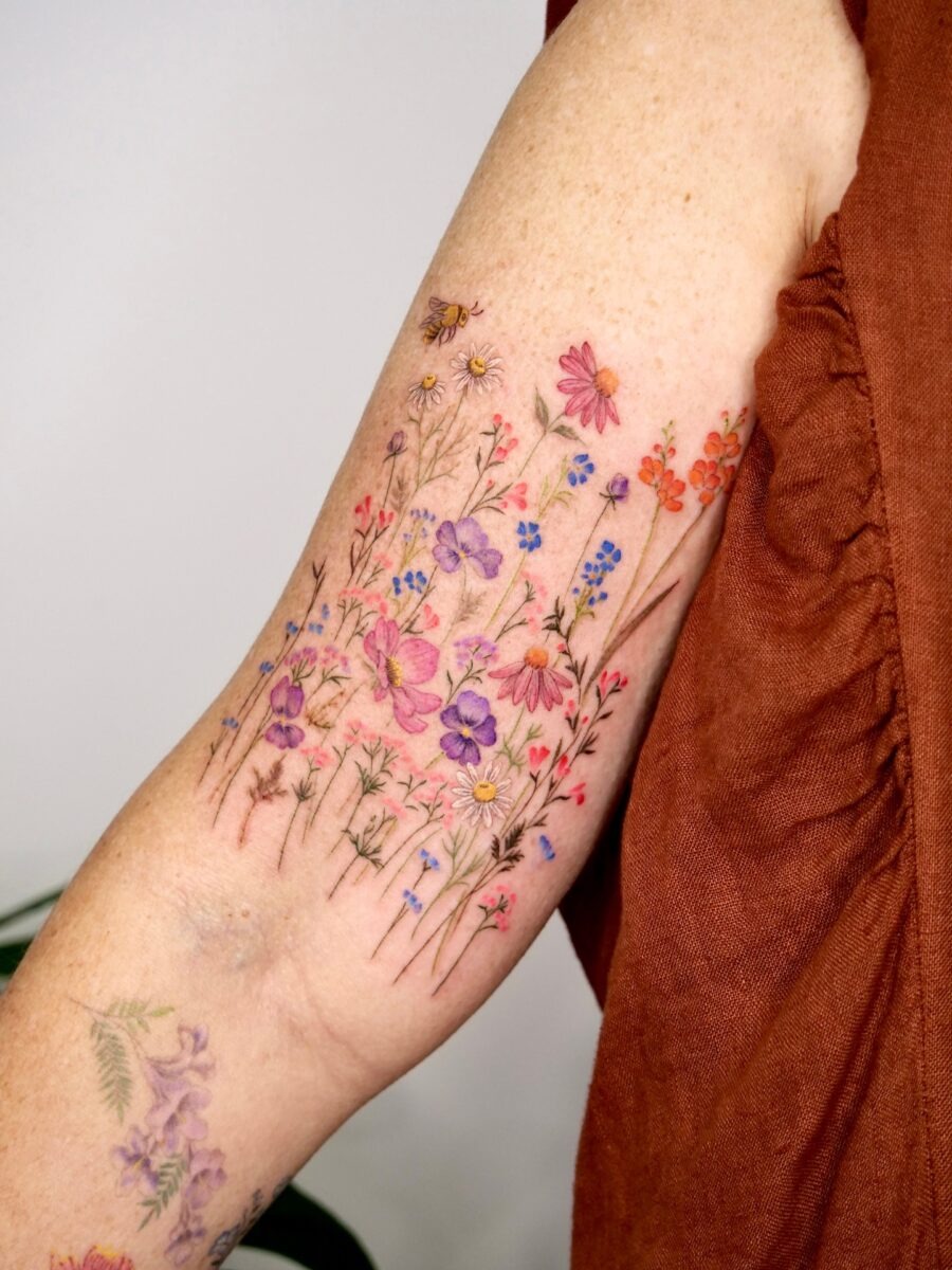 This birth flower tattoo features a variety of delicate flowers scattered across the arm.