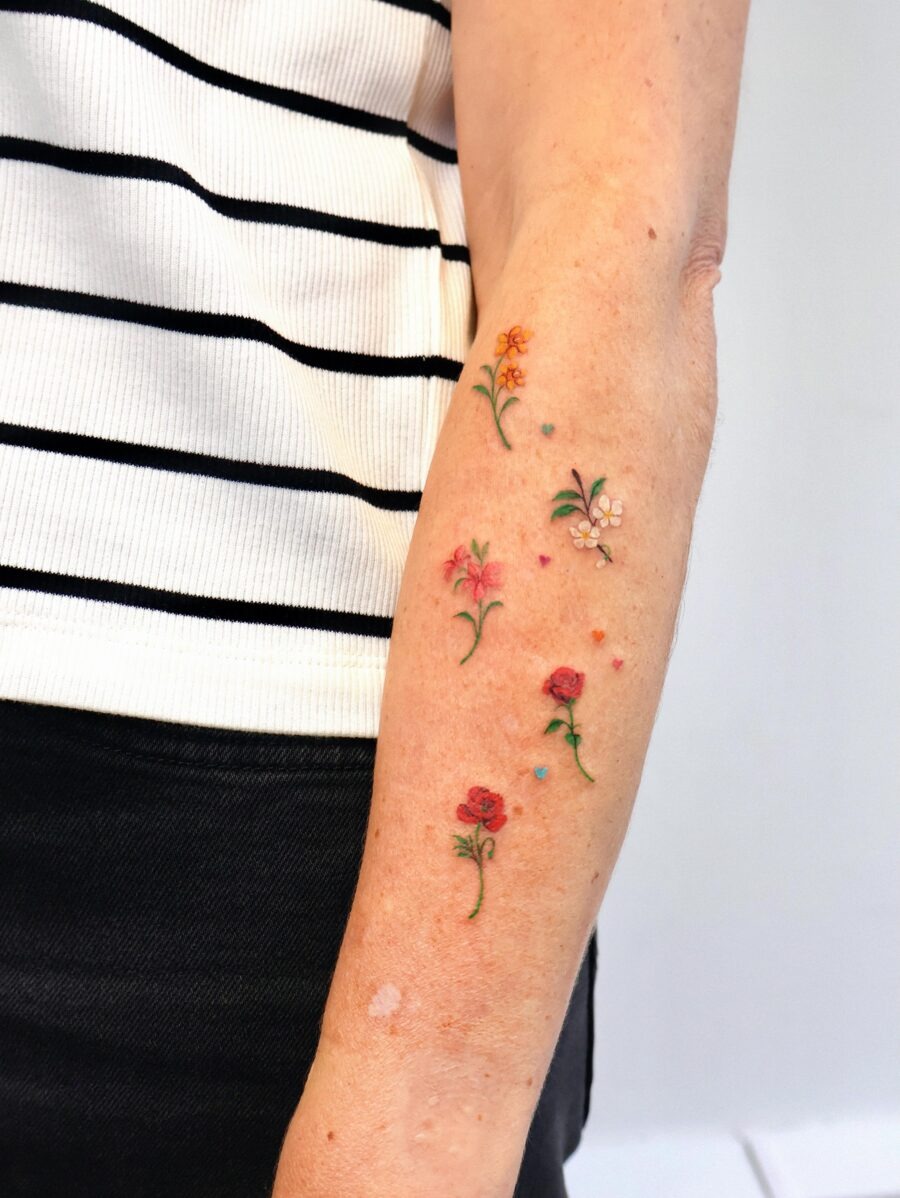 This image showcases an elegant collection of colorful birth flower tattoos on a forearm.