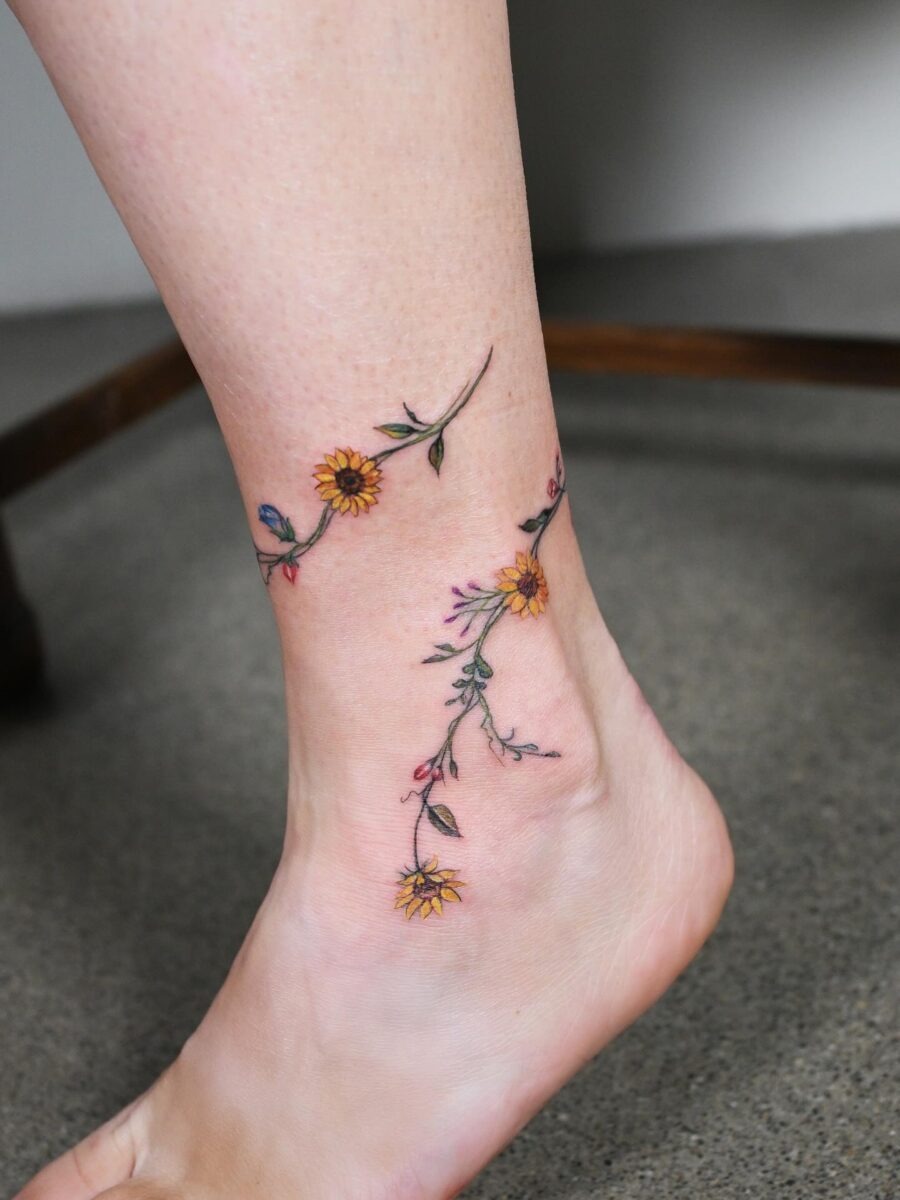 This beautiful tattoo features a winding vine of bright flowers encircling the ankle.