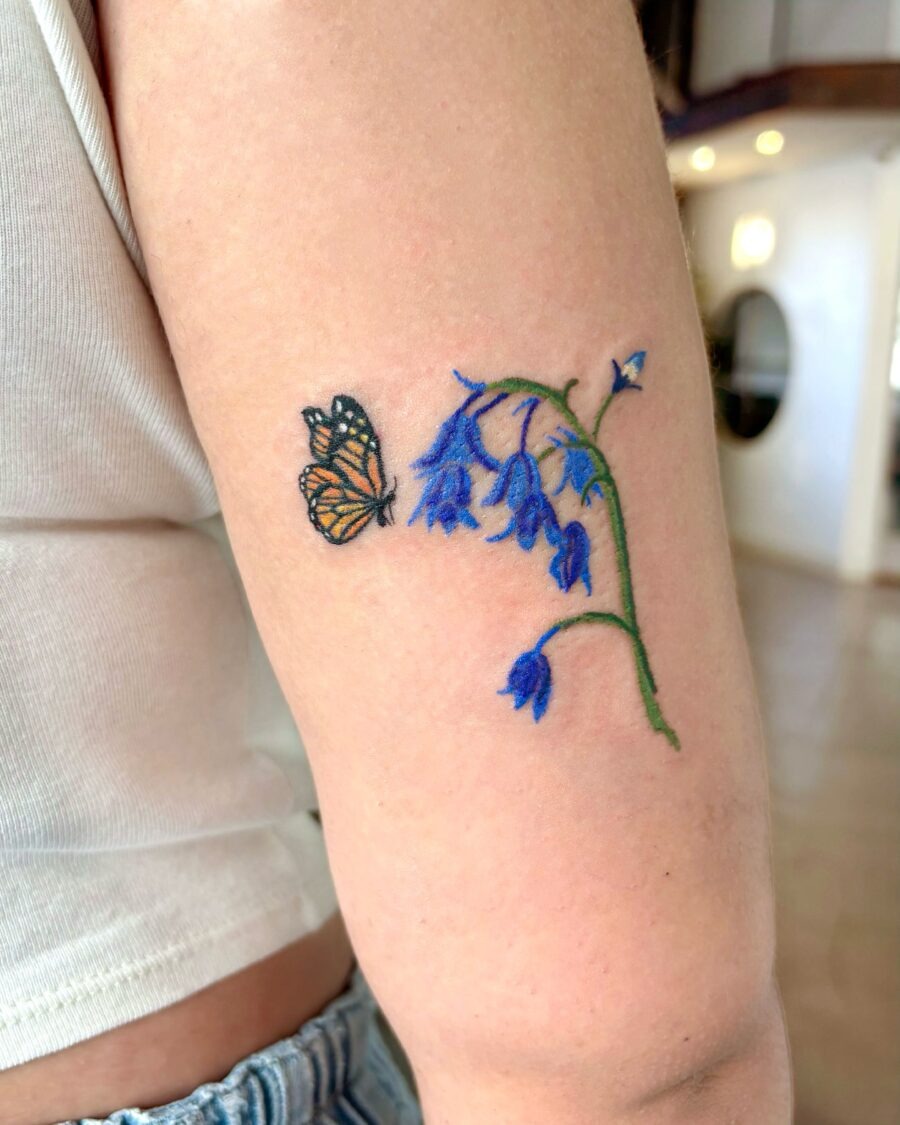 This tattoo features a delicate bluebell flower artfully intertwined with a butterfly.
