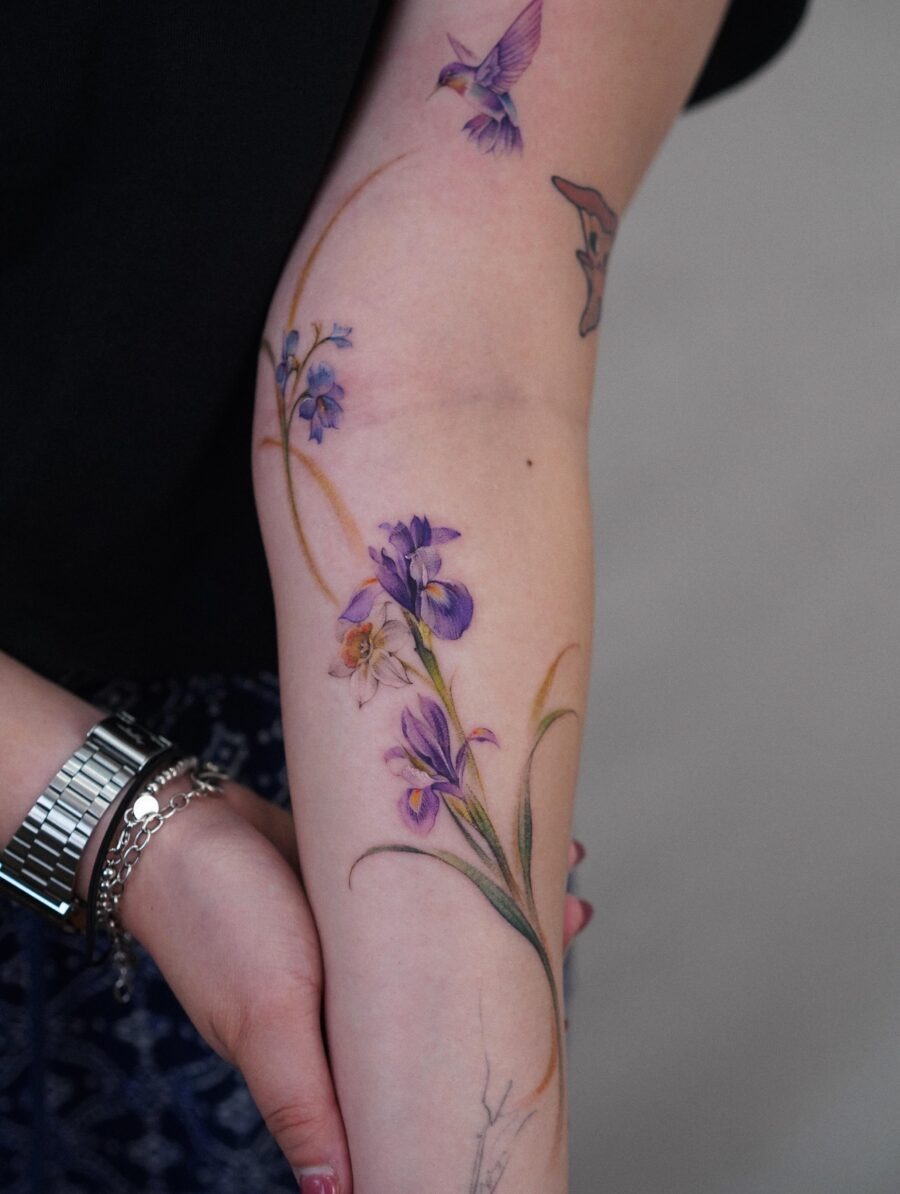 This tattoo features a stunning arrangement of irises, beautifully colored in shades of purple and yellow.