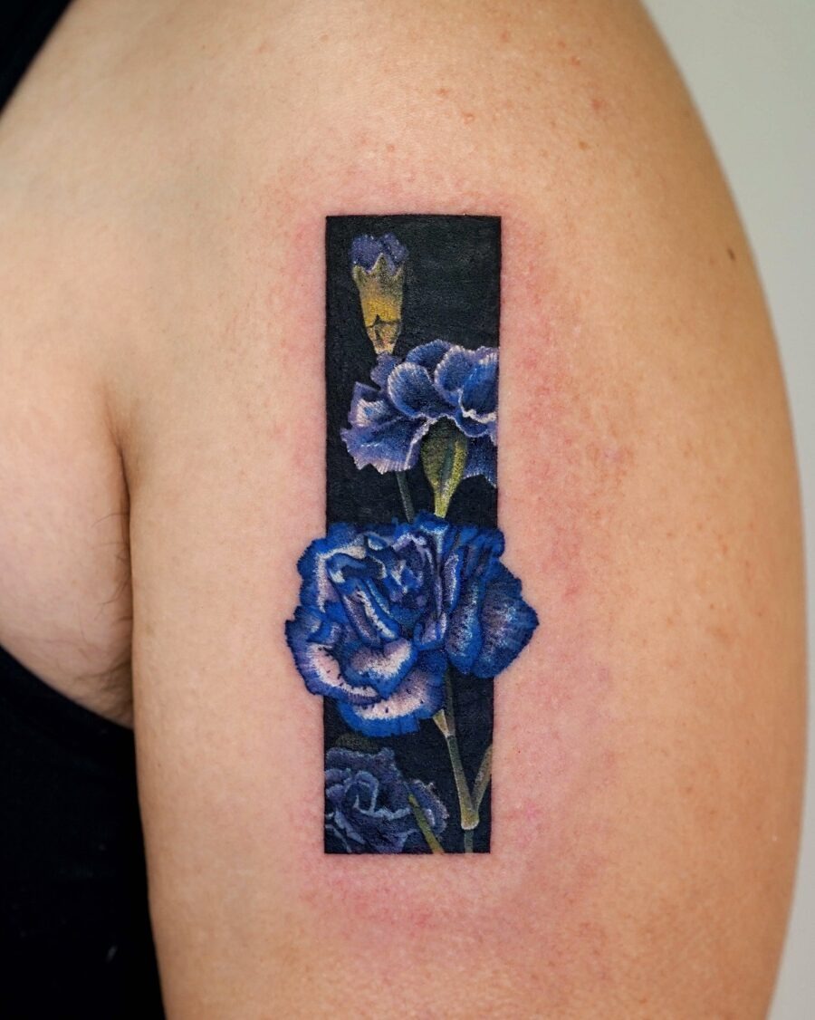 This striking tattoo showcases a cluster of blue carnations framed by a dark background.