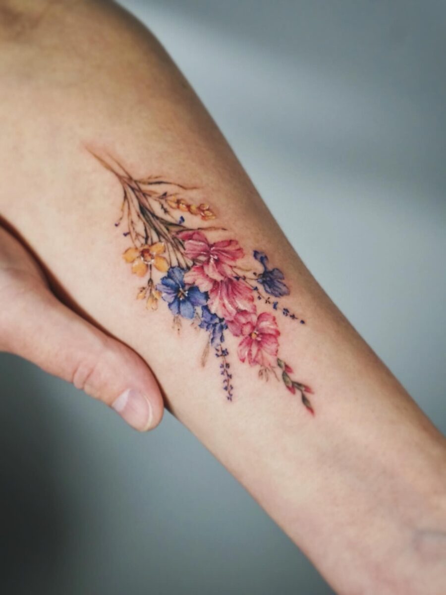 This elegant birth flower tattoo features a delicate arrangement of colorful blooms on the forearm.