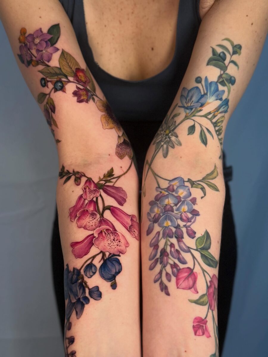 This tattoo design showcases birth flower motifs elegantly wrapping around each arm.