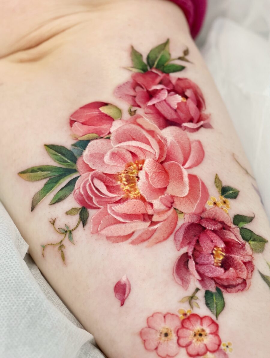 This peony tattoo features lush, blooming flowers in shades of pink and red, beautifully inked on the skin.