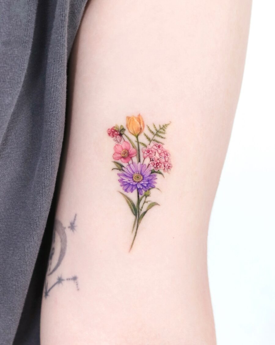 This tattoo showcases a beautiful arrangement of birth flowers, combining shades of pink, orange, and purple.