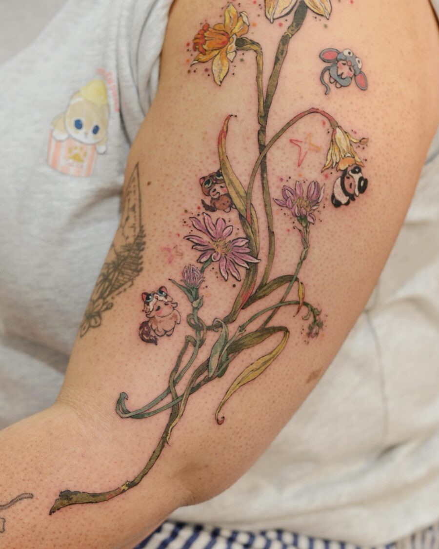This tattoo showcases a design of blooming flowers intertwined with cute, whimsical characters.