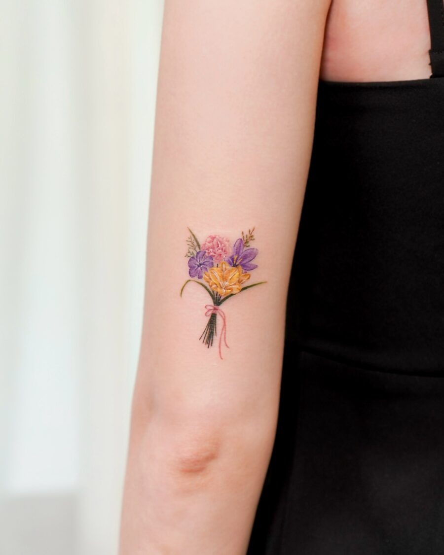 This stunning tattoo features a bouquet of various birth flowers, including rich purple and soft pink hues.
