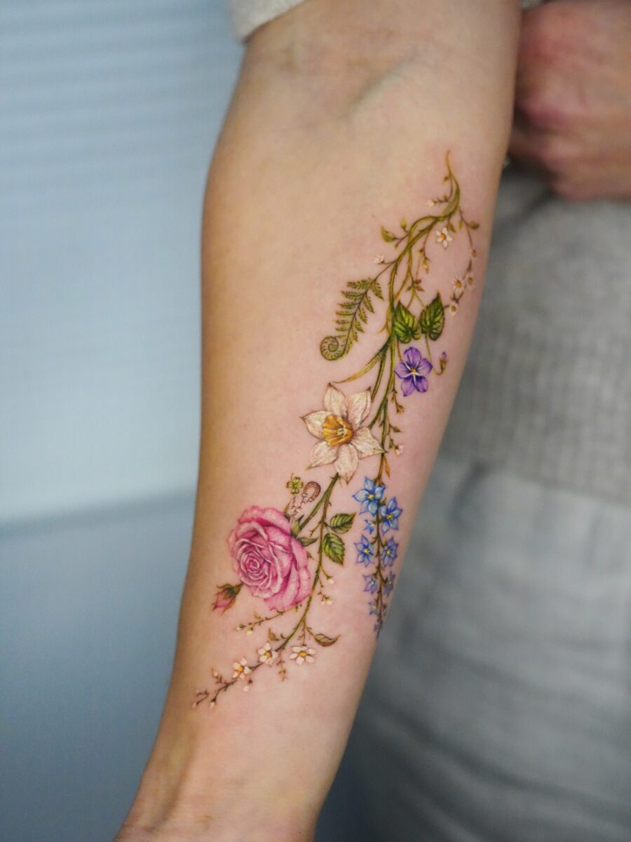 This stunning tattoo features an intricate arrangement of flowers, showing roses and delicate blossoms entwined with graceful vines.