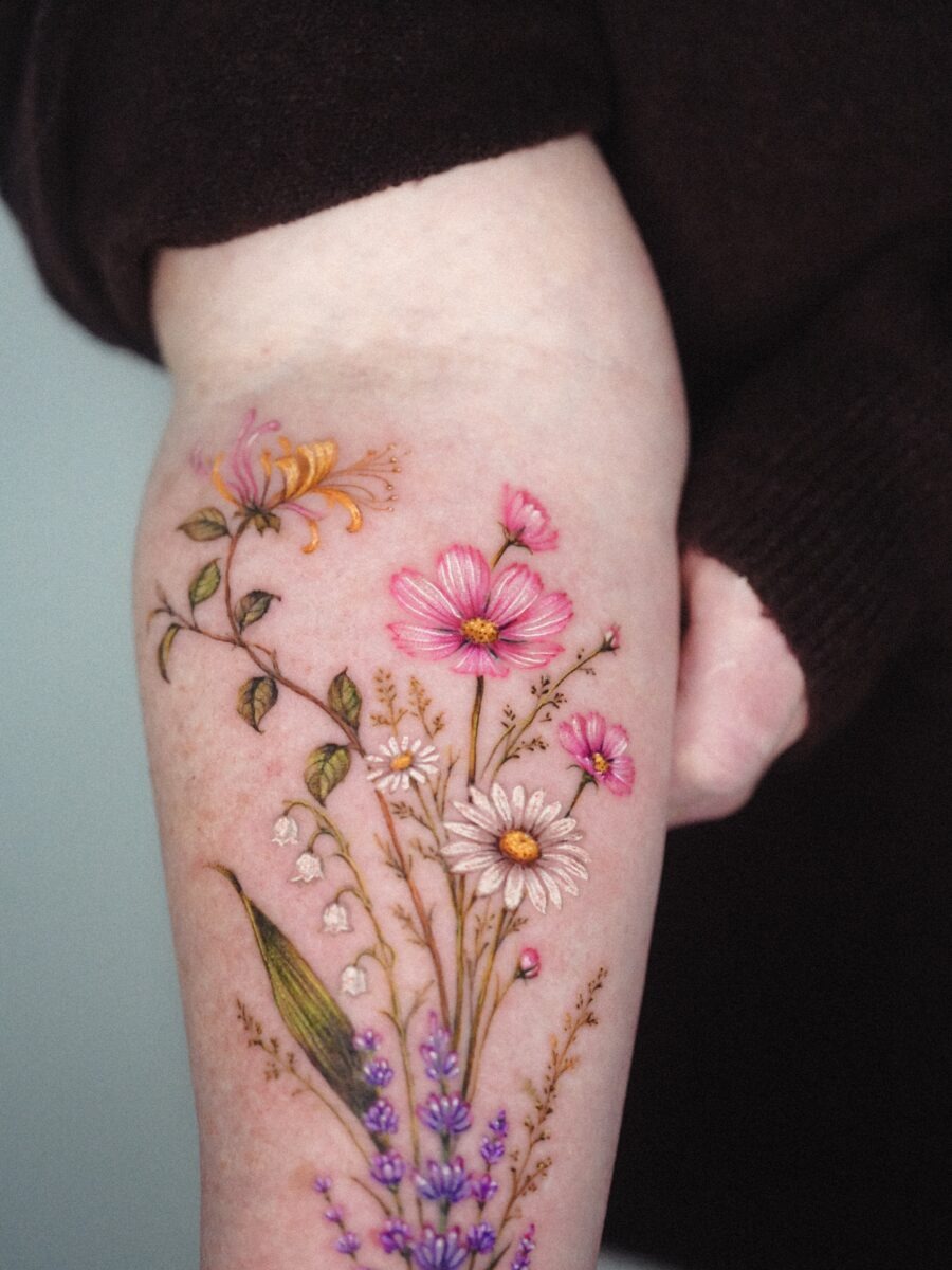 This tattoo beautifully features an array of colorful flowers, including daisies and lavender.