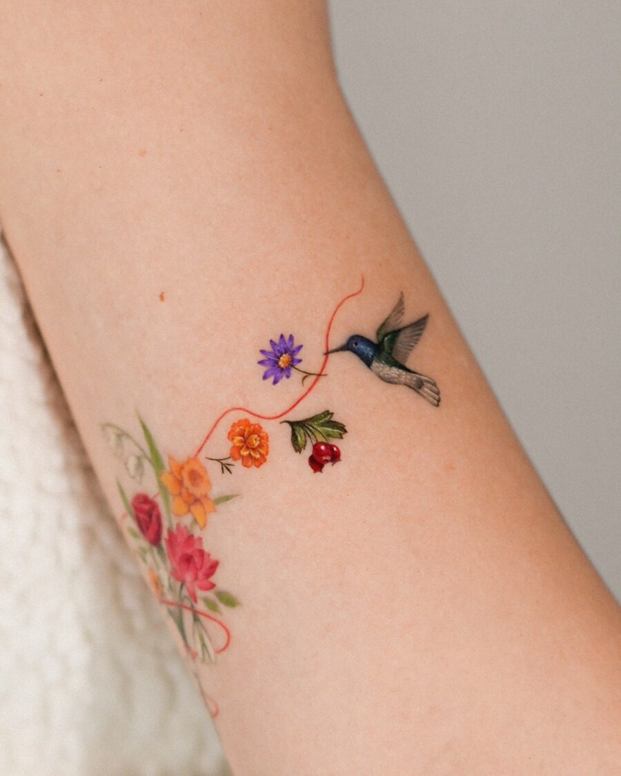 This stunning tattoo features a delicate hummingbird hovering near a array of flowers.