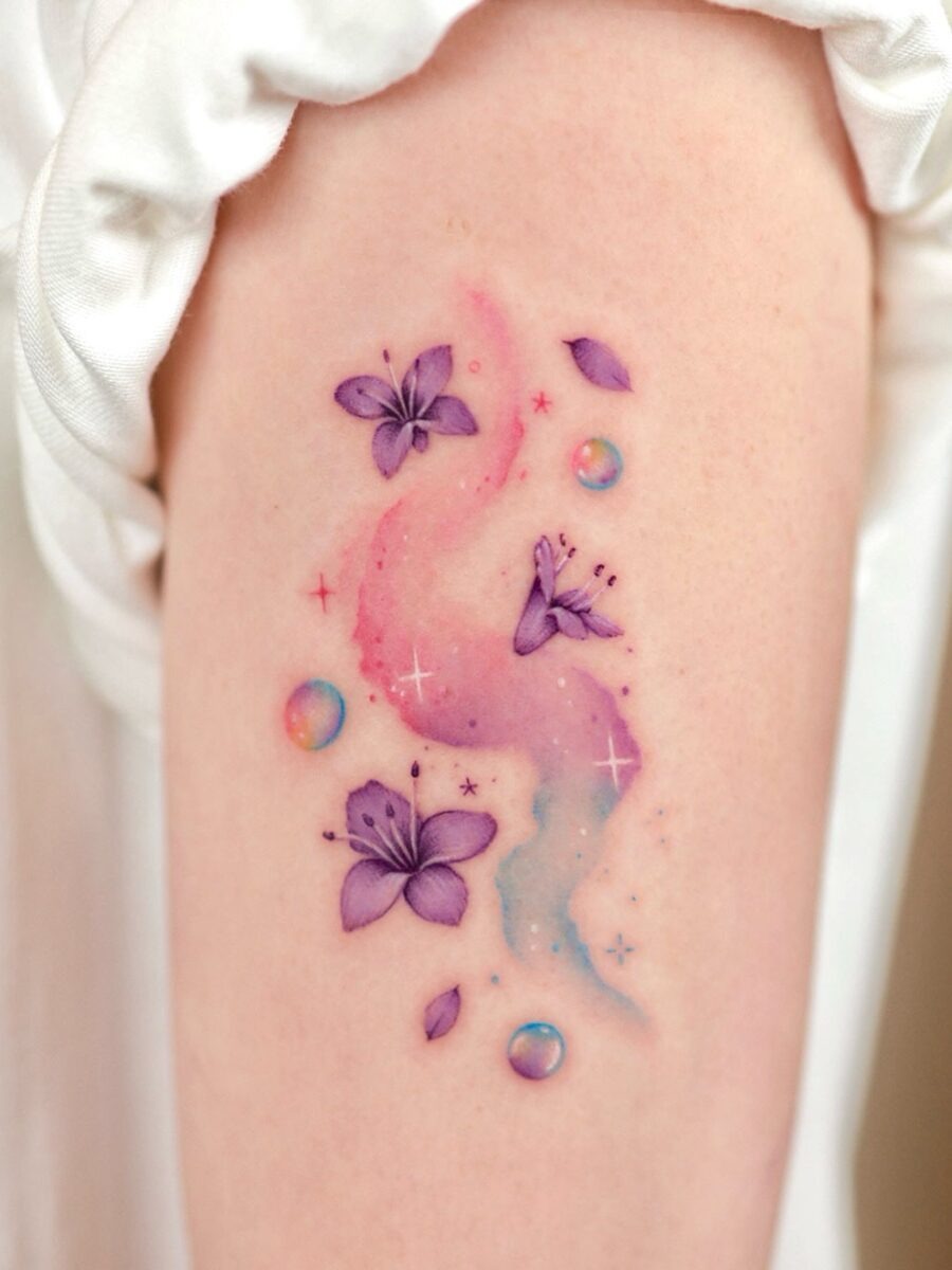 This enchanting tattoo beautifully blends purple flowers with a dreamy pink and blue background.