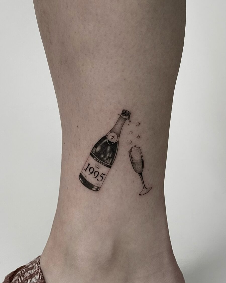 This elegant tattoo features a champagne bottle and glass, symbolizing celebration.