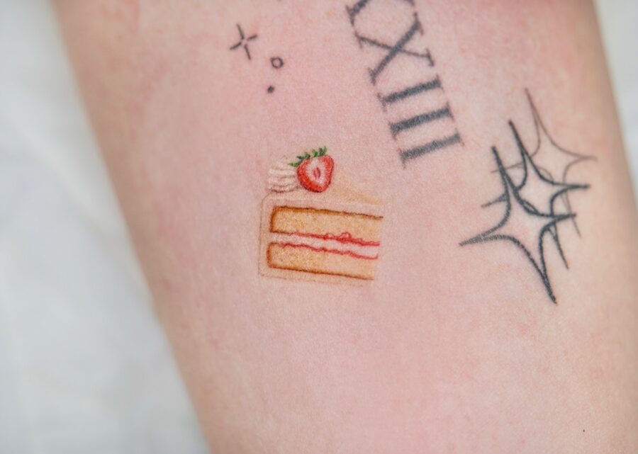 This charming tattoo features a slice of cake topped with a strawberry, capturing the essence of celebration.