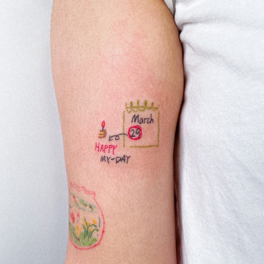 This colorful tattoo features a birthday calendar and cake drawn on the arm.