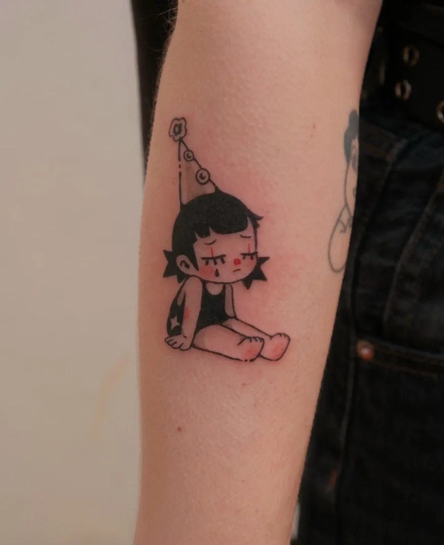 This tattoo features a playful character wearing a party hat, exuding a whimsical vibe.