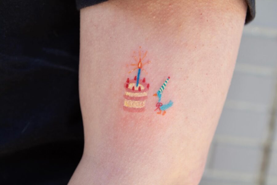 This tattoo features a whimsical birthday cake adorned with a lit candle.