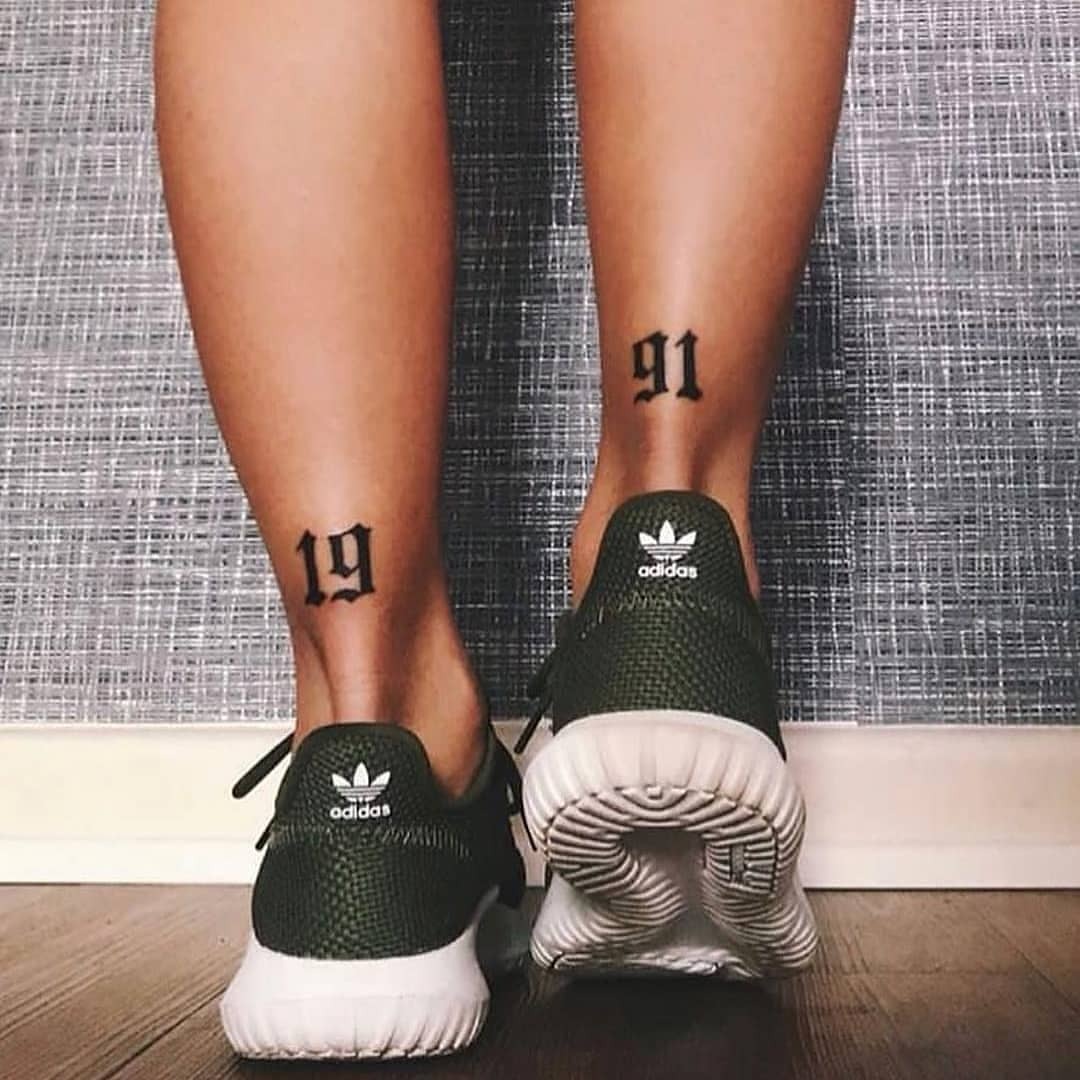 This tattoo features bold numbers '19' and '91' inked on the lower leg, creating a striking visual impact.