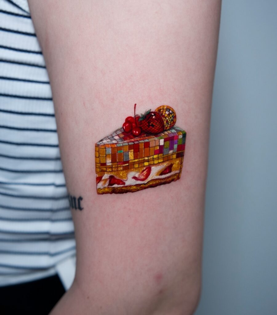 This tattoo features a delectable cake slice adorned with cherries and colorful decorations.