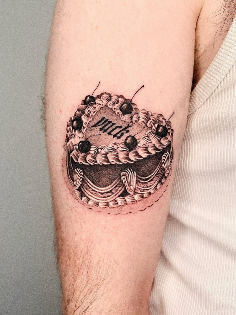 This tattoo features a beautifully detailed birthday cake with intricate frosting and cherries.