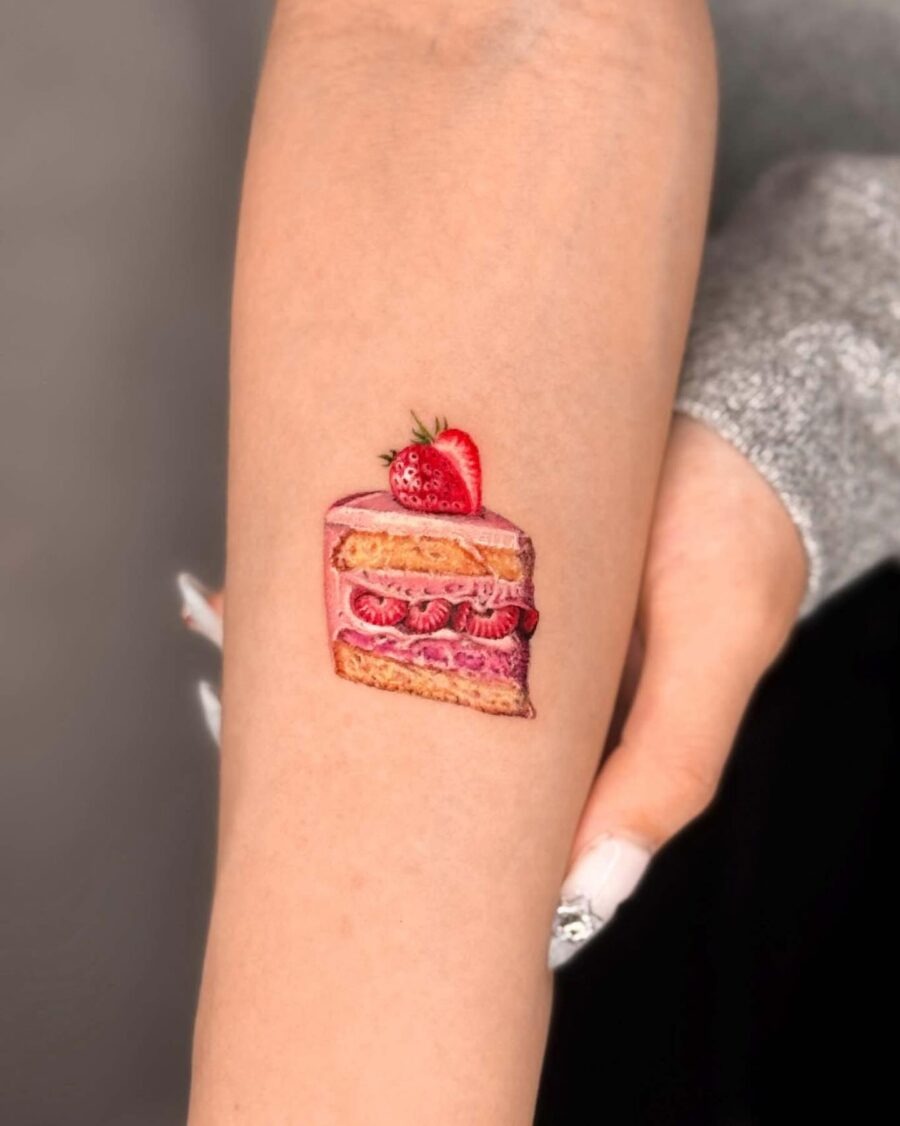 This charming tattoo features a colorful slice of cake topped with a fresh strawberry, beautifully detailed.