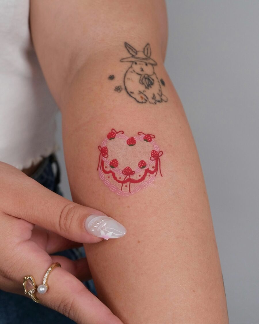 This playful tattoo features a charming cake adorned with ribbons and flowers, representing celebration and joy.
