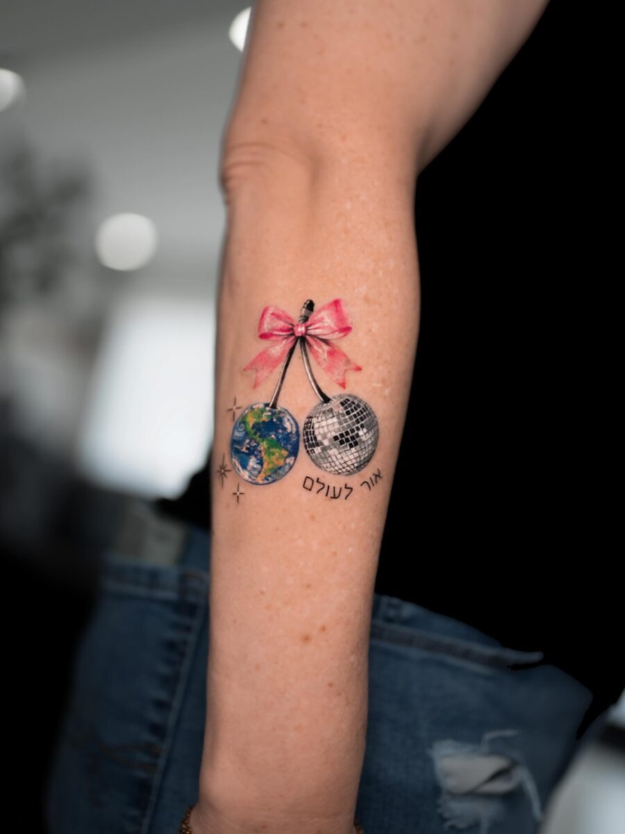 This tattoo features a globe dangling with a charming bow and playful disco ball.