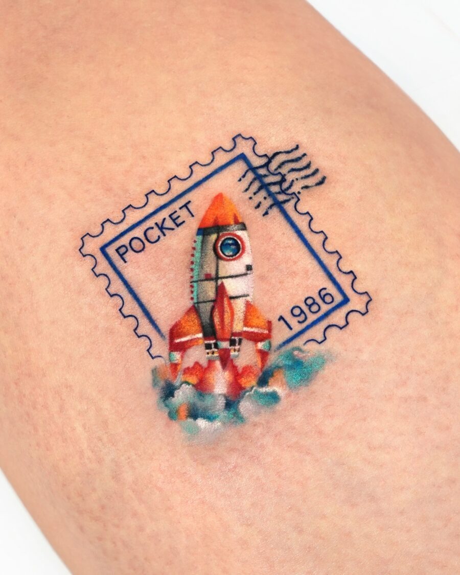 This unique birthday tattoo features a rocket launching from a vintage postage stamp.
