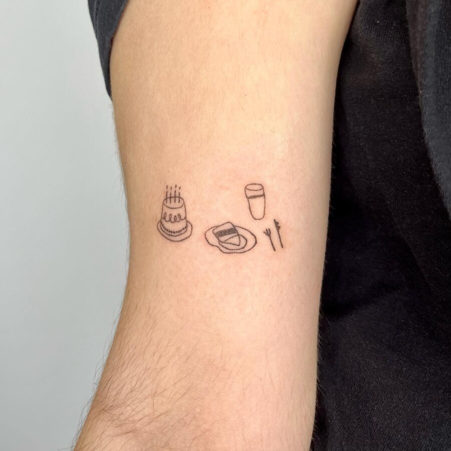 This tattoo showcases a quaint celebration theme with a cake, a glass, and utensils in a minimalist style.