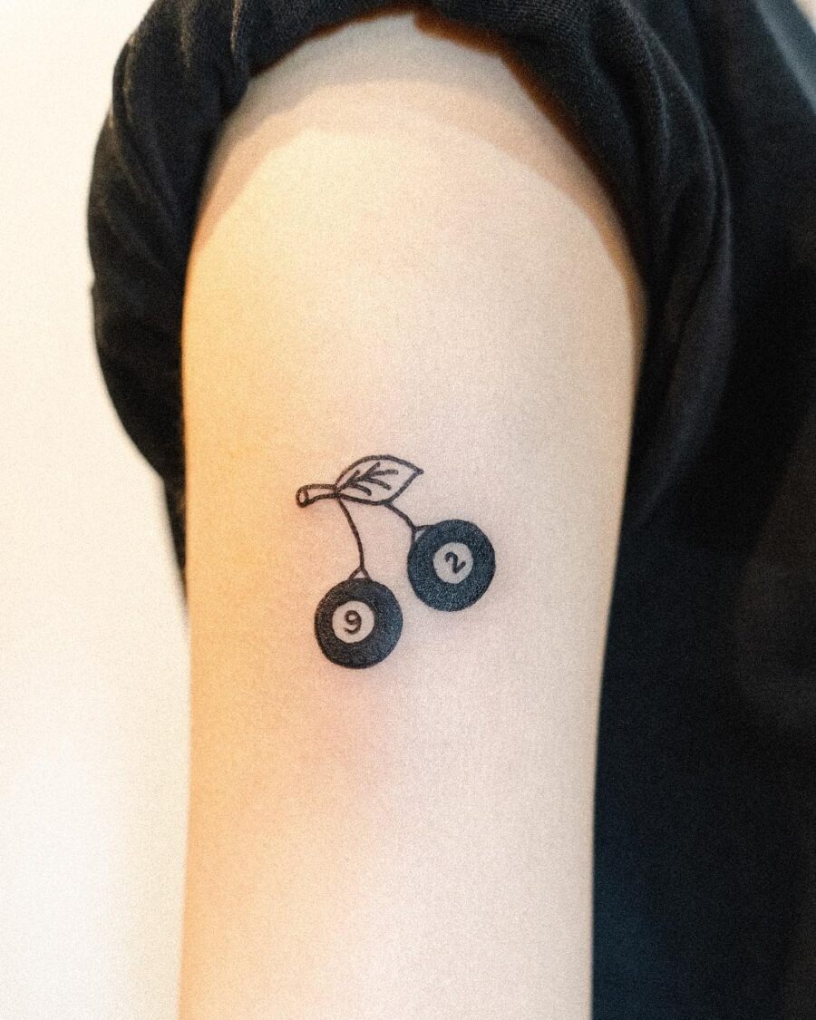 This tattoo features a simple yet charming design of two cherries, each marked with a number that likely signifies a special birthday.