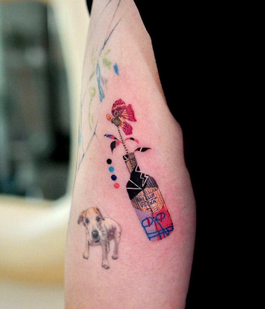 This tattoo features a playful mix of a whimsical bottle and a cute dog, adorned with colorful flowers and abstract shapes.