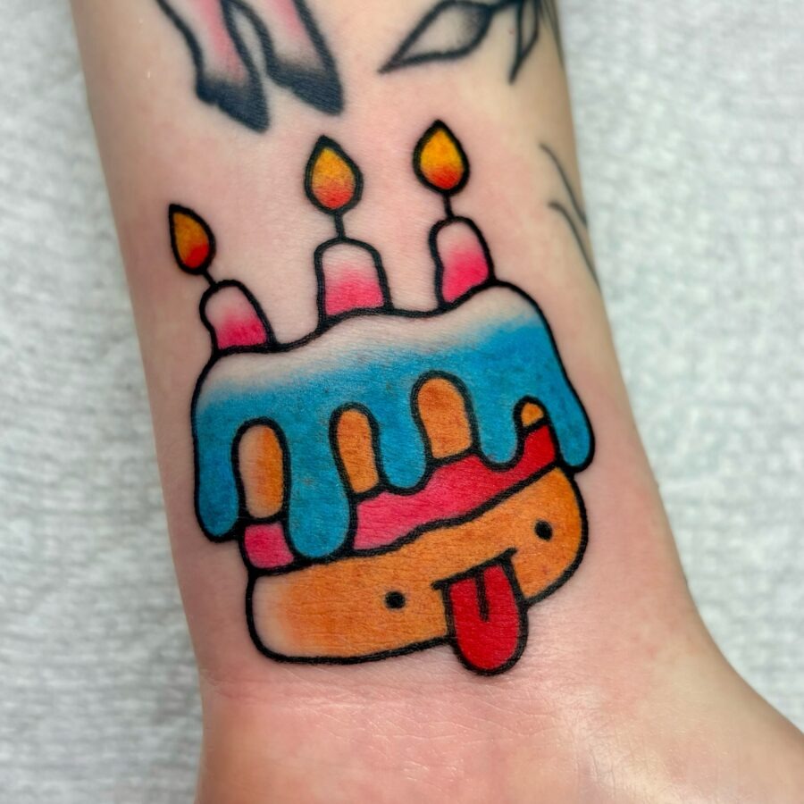 This tattoo features a cartoonish birthday cake topped with colorful frosting and candles.