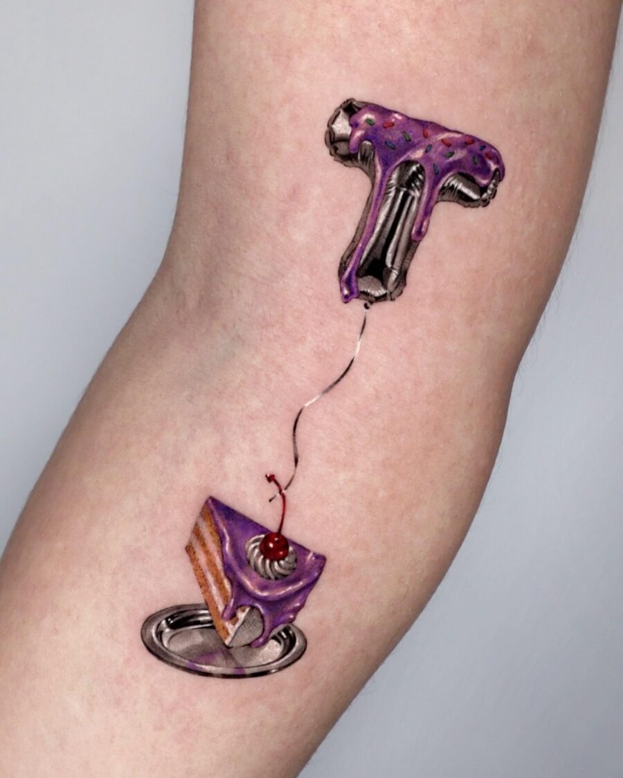 This tattoo showcases a playful slice of cake topped with purple frosting and a cherry.