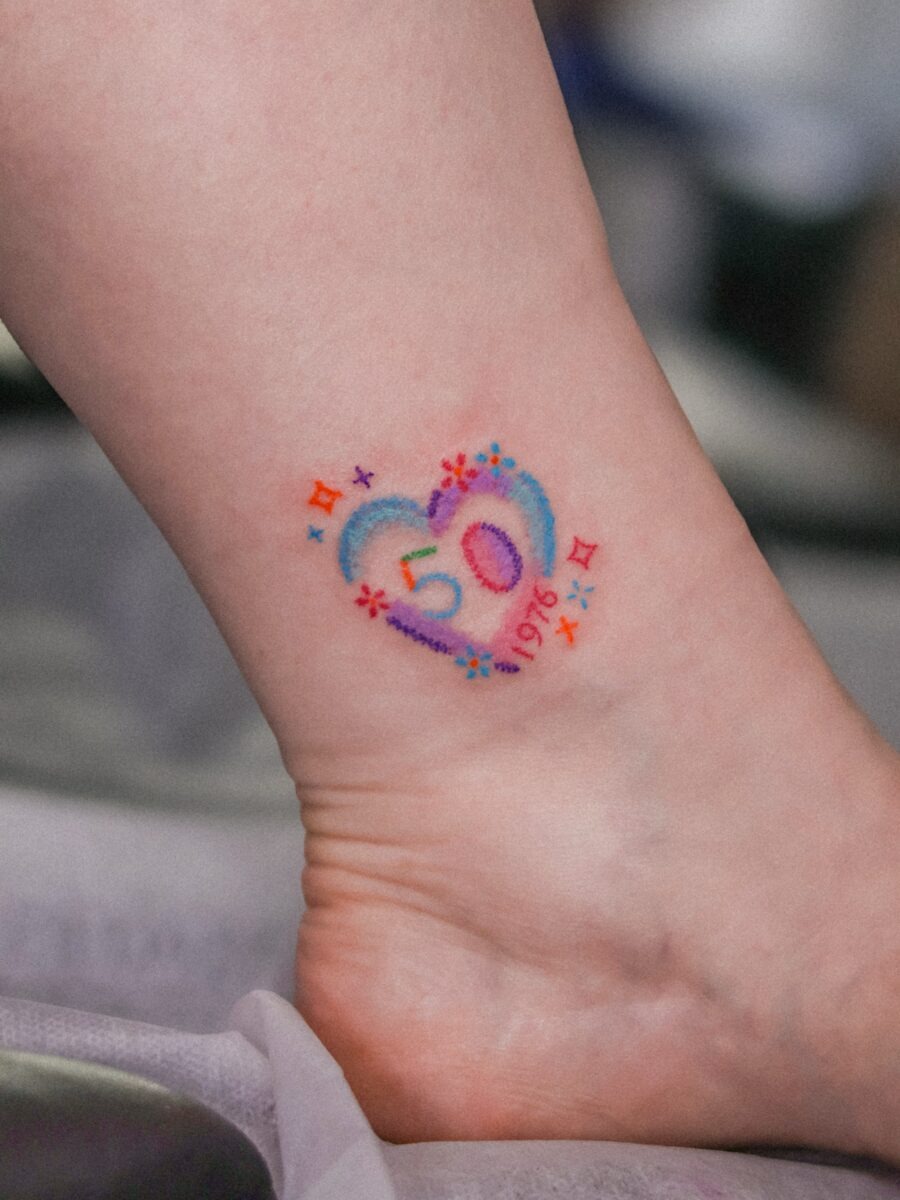 This tattoo features a heart encasing the number 50, surrounded by stars and floral elements.
