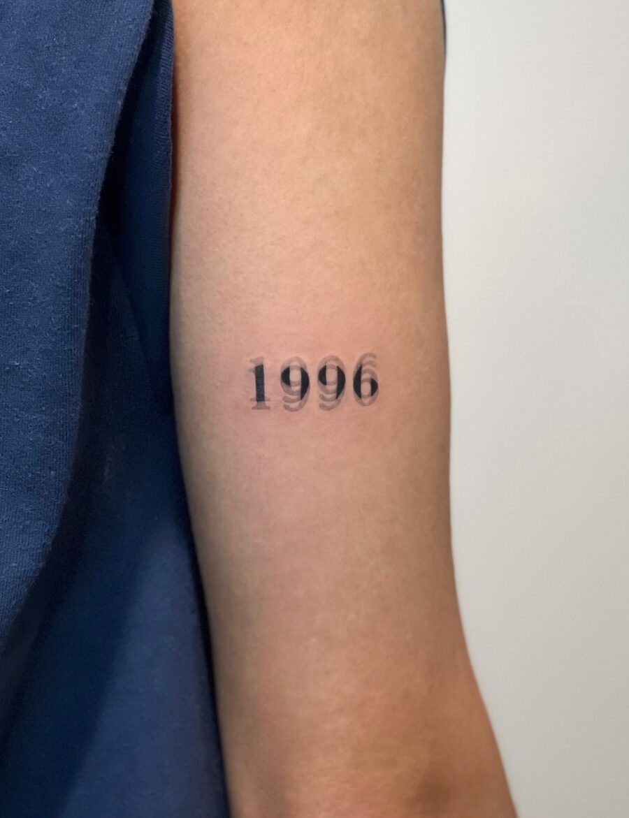 This tattoo features the year '1996' emblazoned in a modern, minimalist style.