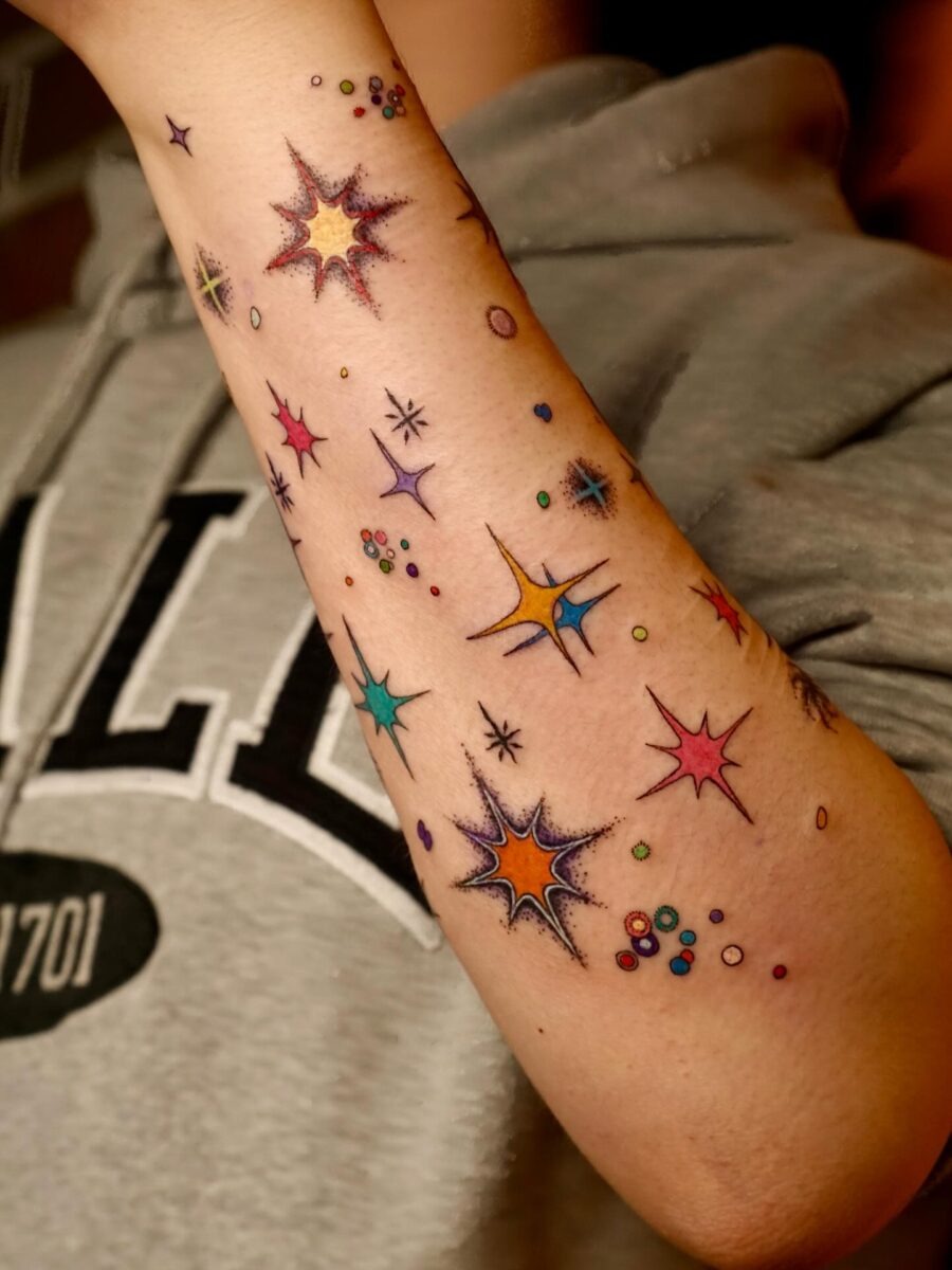 This tattoo bursts with colors and playful star designs, creating a cosmic feel.