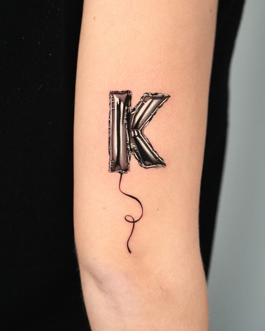 This birthday tattoo features a playful balloon letter K, giving off a festive vibe.
