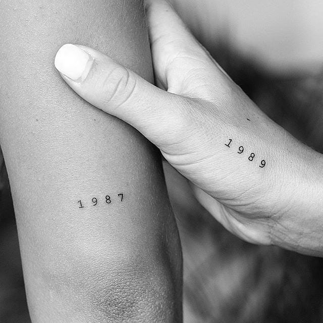 This image features two sleek tattoos displaying the years 1987 and 1989, showing a minimalist aesthetic.