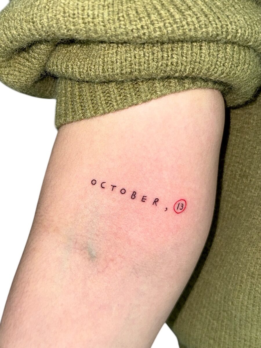 This tattoo features the date 'October 13' in a sleek, minimalist style.