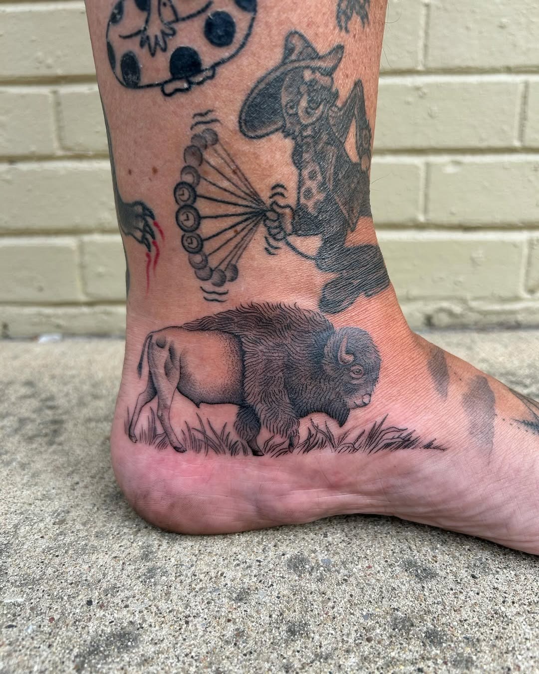 This tattoo showcases a beautifully detailed bison grazing in tall grass, nestled elegantly on the ankle.
