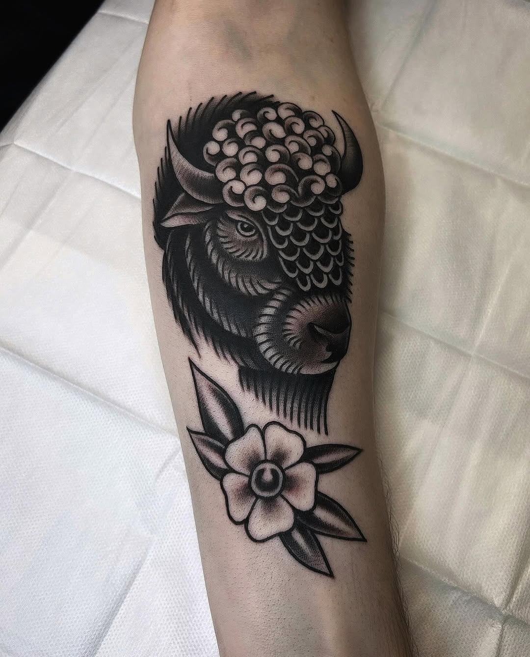 This striking bison tattoo features intricate blackwork details and a beautiful flower, blending power with nature.