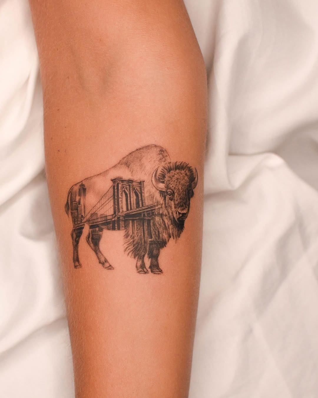 This bison tattoo features a stunning blend of a mighty bison and an iconic city landscape.
