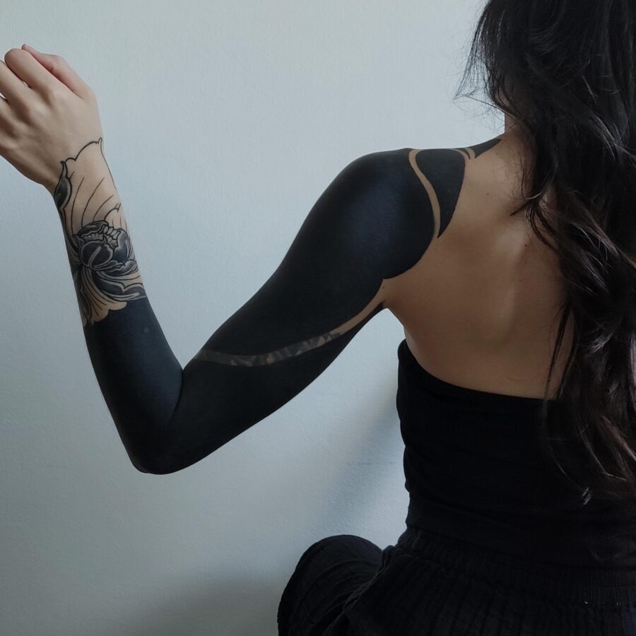 This striking black sleeve tattoo features a blend of intricate designs and solid black areas.