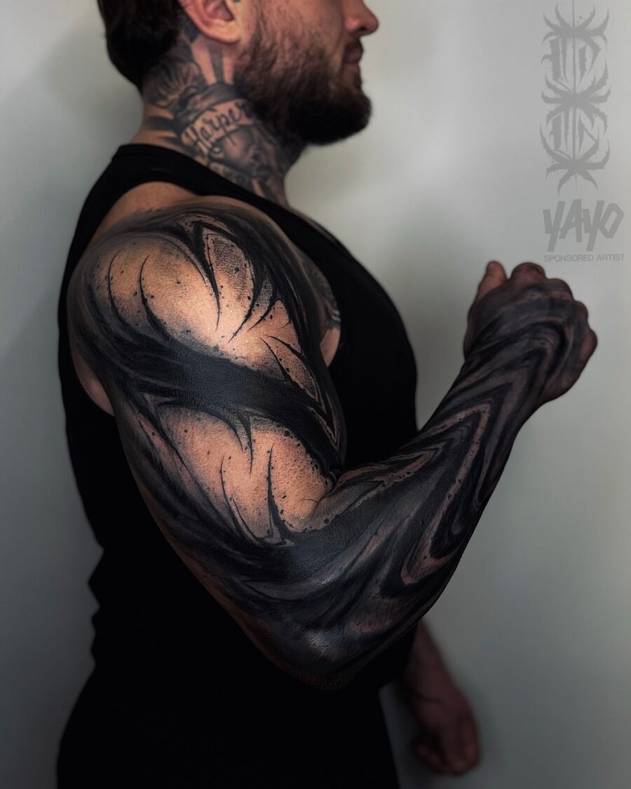 This striking black sleeve tattoo showcases a muscular arm adorned with intricate, swirling designs.